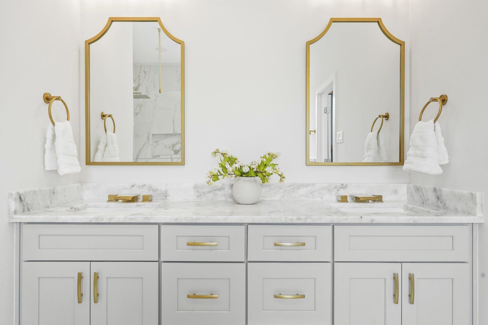 White double vanity with marble top, arched gold mirrors and brass hardware