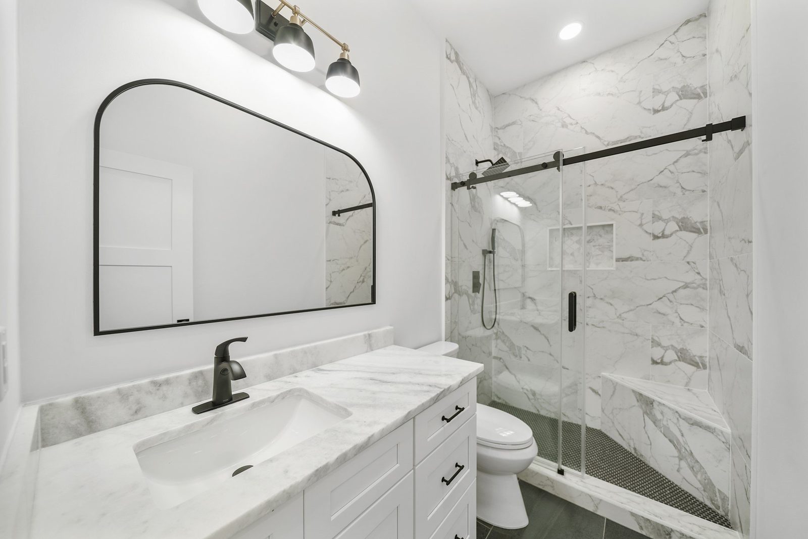 Guest bathroom with a black arched mirror, white vanity and marble-look sliding-door shower